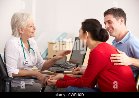 British GP talking to happy couple in surgery Stock Photo