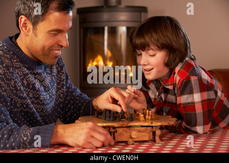 Father And Son Playing Chess By Cosy Log Fire Stock Photo