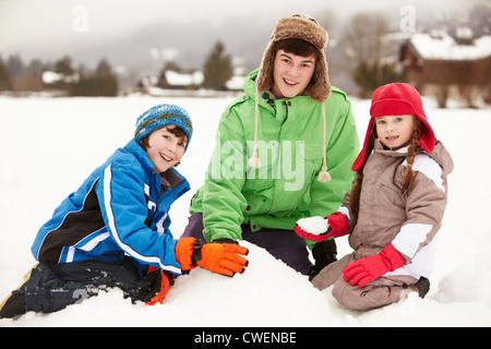 Group Of Children Building Snowman Wearing Woolly Hats Stock Photo