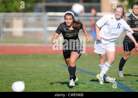 Soccer player rushes after a loose ball to secure the ball during a high school match. USA. Stock Photo