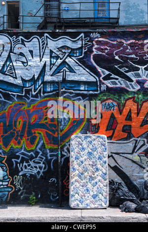 Abandoned mattress leaning against a brick wall covered with graffiti Stock Photo