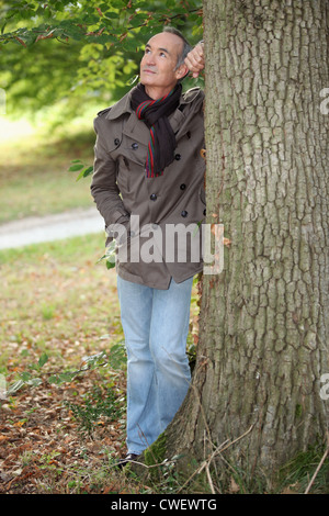 Elderly man leaning against tree Stock Photo