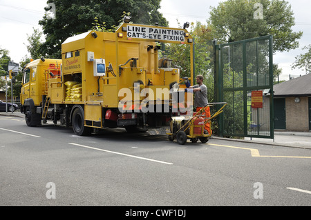 Yellow line painting vehicle with fire going on truck bed to heat material and worker drawing fresh heated lime into bucket Stock Photo
