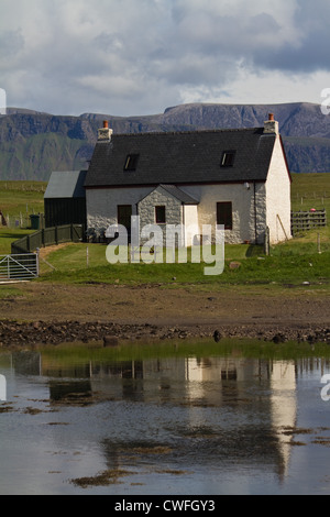A traditional white crofting cottage on the Isle of Canna, Small Isles, Scotland, reflected in the waters of the bay Stock Photo