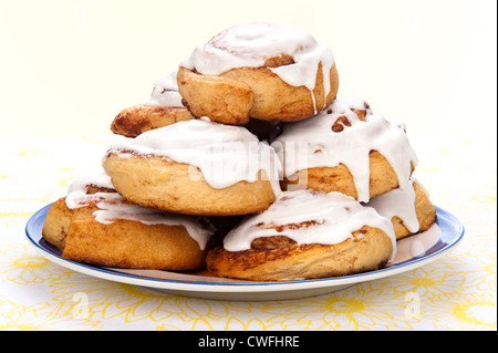 A plate of freshly baked cinnamon rolls with sweet, white icing dripping down the sides. Stock Photo