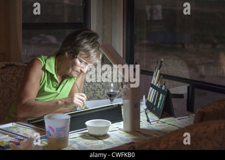 Mature woman relaxes with a glass of wine while working on her watercolour painting Stock Photo