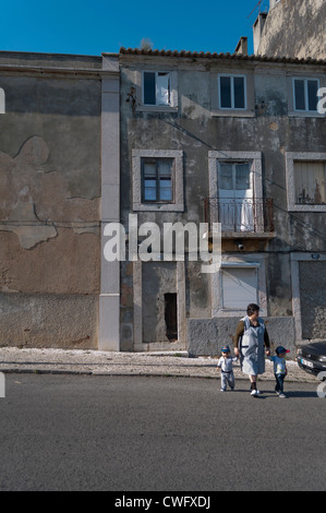 Woman holding hands with two little boys in front of old decaying house. Lisbon, Portugal Stock Photo