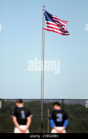Baseball Two players honor the flag during the playing of the Star Spangled Banner prior to the start of a high school game. USA. Stock Photo