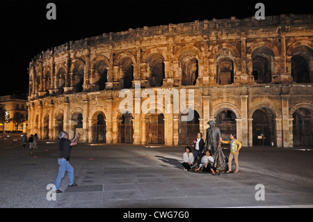 Tourists posing for a photograph in front of Roman amphitheatre or arena Nimes France with floodlights at night Stock Photo