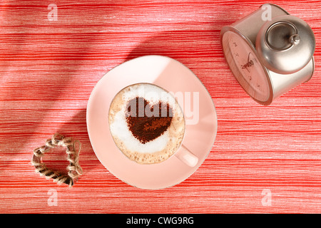 cappuccino with old alarm clock and cocoa heart on red stripy backdrop Stock Photo