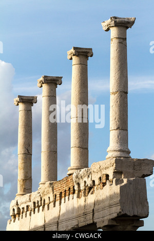 four ionic columns in the Forum of the Roman city of Pompeii, lit by the yellow evening sun against a blue sky. Stock Photo