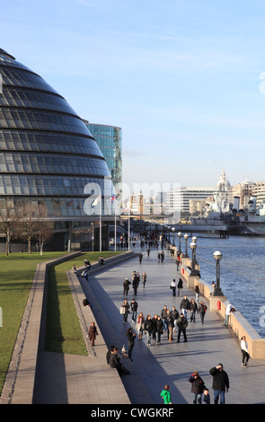Tourists walking along the Queen's Walk, by the river Thames and past City Hall, on a winter's day in London, UK Stock Photo