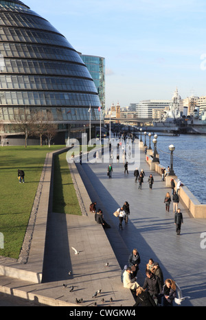 Tourists walking along the Queen's Walk, by the river Thames and past City Hall, on a winter's day in London, UK Stock Photo