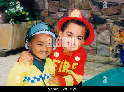 Children outdoors in garden. Two boys dressed-up as firefighter and policeman. Stock Photo