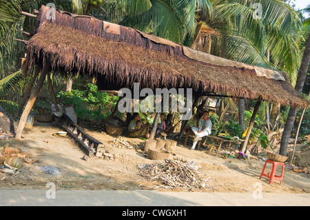 Horizontal view of a family sitting underneath a typical grass shelter on the roadside in rural Cambodia. Stock Photo