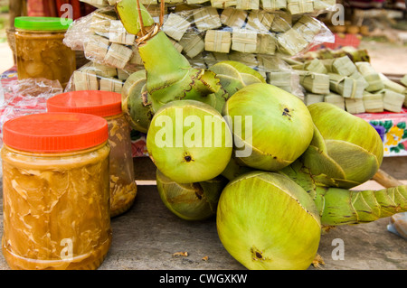 Horizontal close up of tubs of palm sugar, fresh coconuts and the tubes of prepared palm sugar sweets ready to sell on the roads Stock Photo