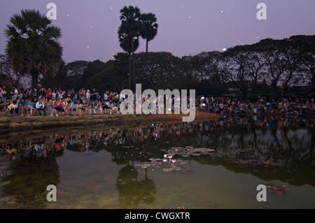 Horizontal view of tourists sitting together around a lake watching the sunrise over Prasat Angkor Wat. Stock Photo