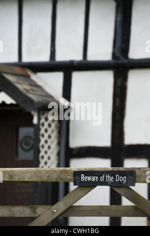 Beware of the Dog sign on a gate in front of an old black and white timber framed house. Herefordshire. England Stock Photo