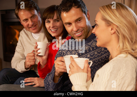 Group Of Middle Aged Couples Sitting On Sofa With Hot Drinks Talking Stock Photo