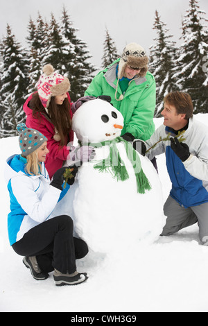 Teenage Family Building Snowman On Ski Holiday In Mountains Stock Photo