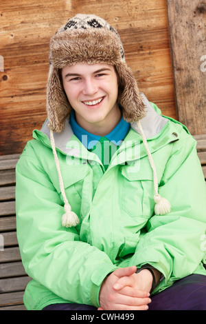 Teenage Boy Dressed For Cold Weather Sitting On Wooden Bench Stock Photo