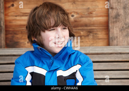 Boy Dressed For Cold Weather Sitting On Wooden Bench Stock Photo
