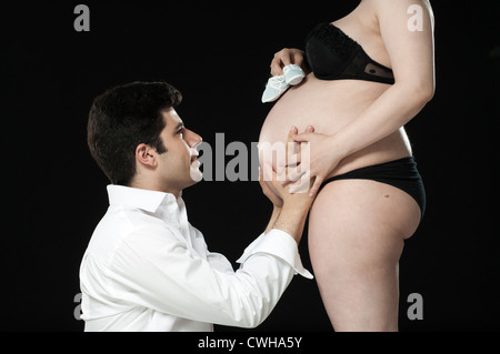 Portrait of young father looking at baby shoes on wife's baby belly. Stock Photo