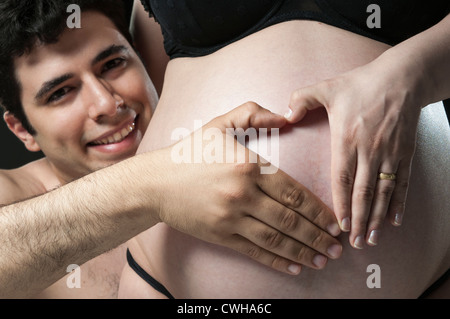 Portrait of young father making the shape of a heart on woman's baby belly and smiling. Stock Photo