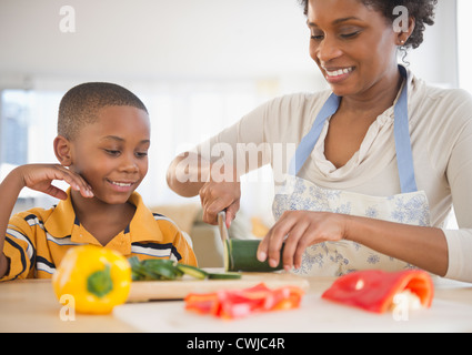 Black son watching mother slicing vegetables Stock Photo