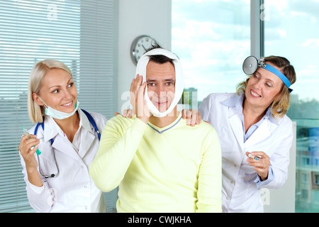 Portrait of two careful female doctors giving first aid to male patient with toothache in hospital Stock Photo