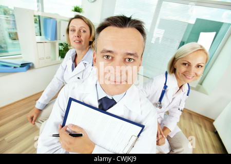 Portrait of male clinician with clipboard and his two colleagues looking at camera in hospital Stock Photo