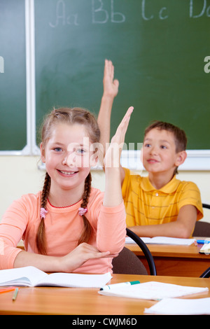 Portrait of lovely girl raising hand at workplace with schoolboy on background Stock Photo