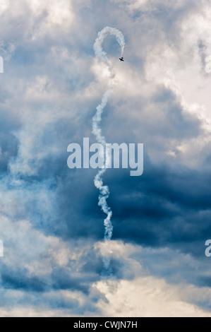 Single plane performing aerial aerobatics with a smoke trail against a moody sky backdrop. Stock Photo