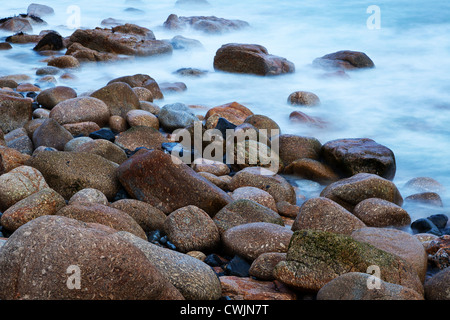 Long exposure photo of large boulders with the sea washing over them, the long exposure has created a misty effect on the water. Stock Photo