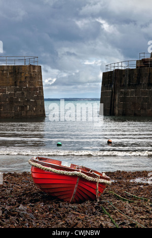 A small red wooden fishing boat moored up in Mousehole harbour Cornwall with storm clouds on the horizon. Stock Photo