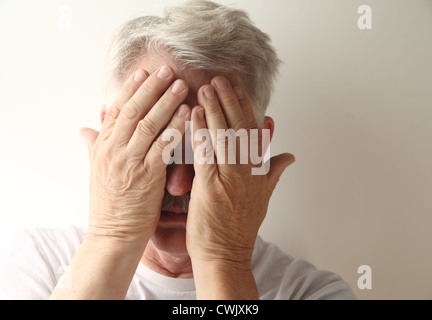an older man hides his face in embarrassment or grief Stock Photo