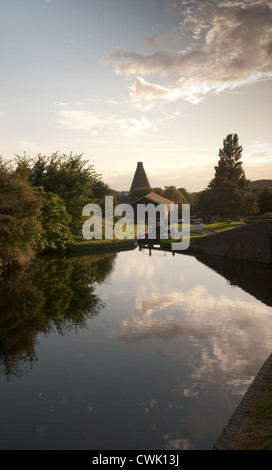 Late summer sun and trees reflected in a canal basin and in front of locks and the historic Red House Glass Cone Stourbridge Stock Photo