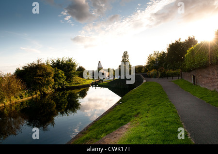 Late summer sun and trees reflected in a canal basin and in front of locks and the historic Red House Glass Cone Stourbridge Stock Photo