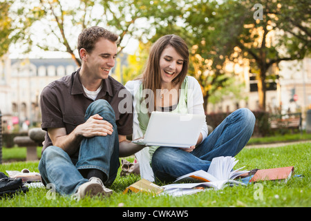 Caucasian students sitting in grass looking at laptop Stock Photo