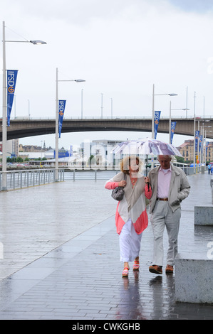 A mature couple walking in the rain on the riverside in Glasgow Stock Photo