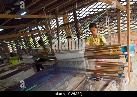 Horizontal close up of women weaving the silk threads into fabric on a loom at a silk producing factory in Cambodia. Stock Photo