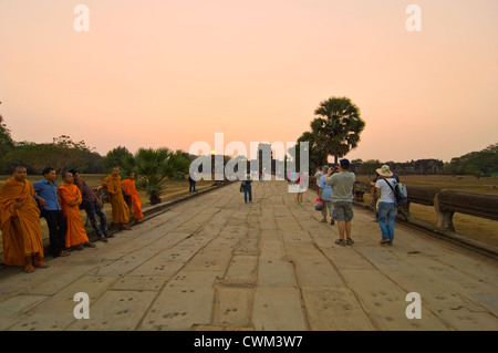 Horizontal view of monks sitting along the Naga causeway in the evening sun at Angkor Wat Stock Photo