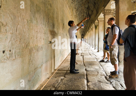 Horizontal view of a guide and a group of tourists standing infront the amazing carvings at Prasat Angkor Wat Stock Photo