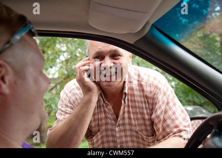 Cheerful enterprising multitasking Polish businessman scheduling car repair while talking on cell phone Rzeczyca Central Poland Stock Photo