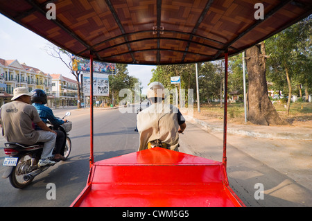 Horizontal view from inside a tuk-tuk travelling down a road in Cambodia with a motorbike riding alongside. Stock Photo