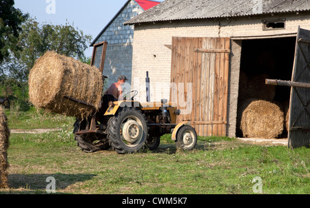 Farmer loading large round bails of hay into the barn with a rear lifting tractor. Zawady Central Poland Stock Photo