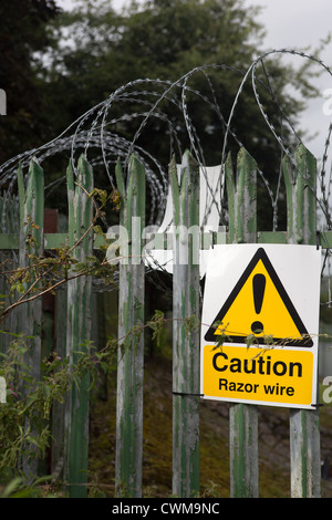 A warning sign on a security fence topped with razor wire Stock Photo
