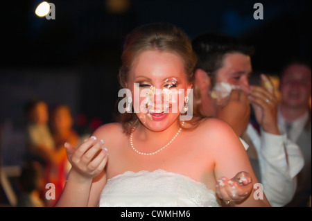 Bride and groom smearing each others faces with icing during a traditional cake cutting ceremony at their American wedding. Stock Photo