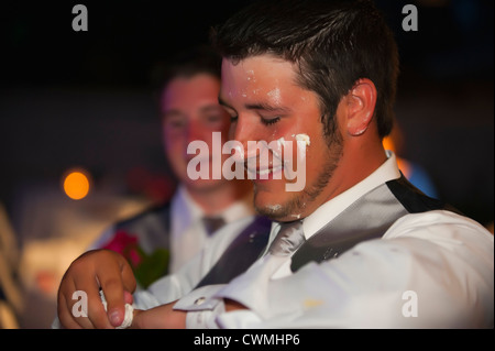 Bride and groom smearing each others faces with icing during a traditional cake cutting ceremony at their American wedding. Stock Photo