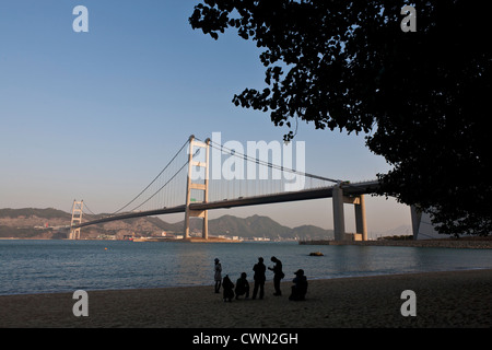 Youths play on a beach against a backdrop of the Tsing Ma suspension bridge in Hong Kong. Stock Photo